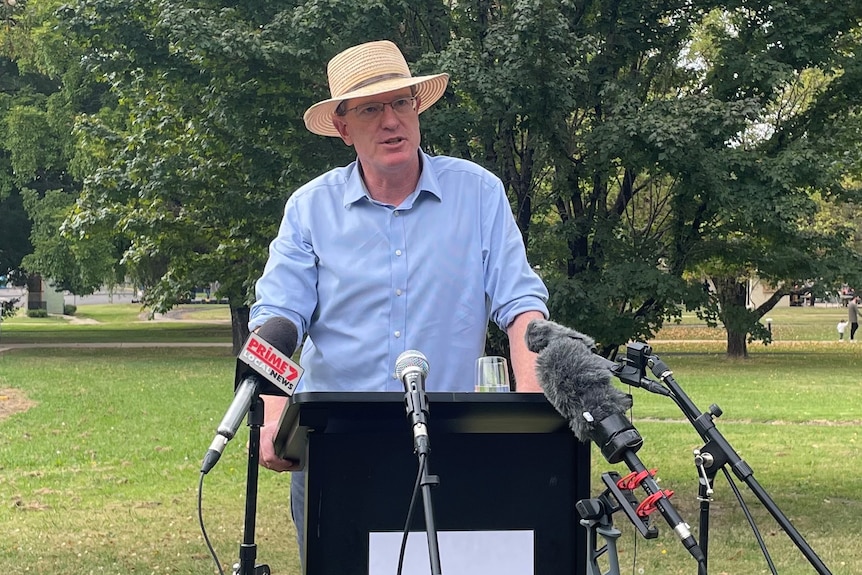 A man in a hat stands at a lectern