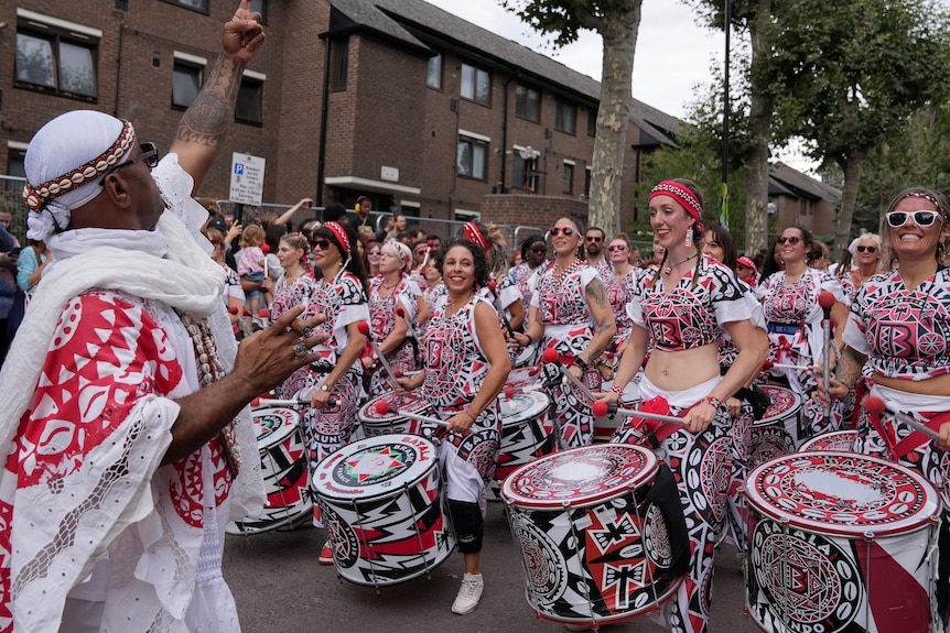 Dozens of performers wearng red and white costumes are beating drums. 