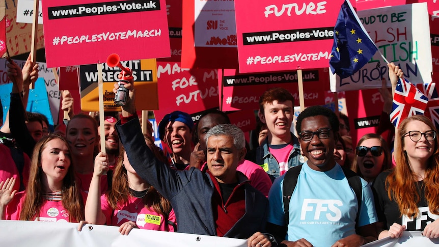 Mayor of London Sadiq Khan stands in a crowd of people holding red signs calling for a people's vote on Brexit.