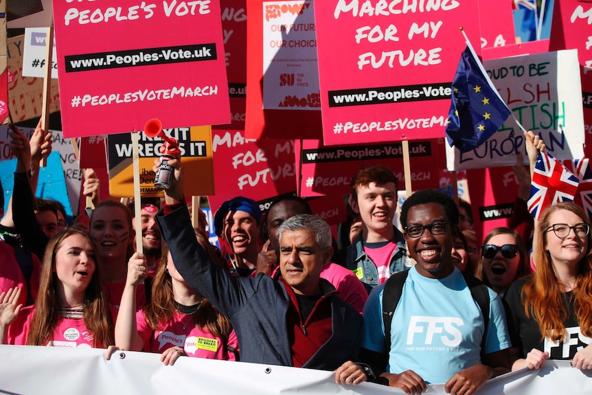 Mayor of London Sadiq Khan stands in a crowd of people holding red signs calling for a people's vote on Brexit.