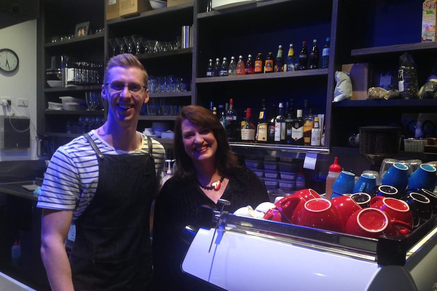 Two people stand behind a coffee machine in a cafe