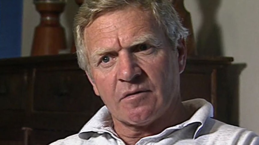 A stern looking man in a white polo shirt. 