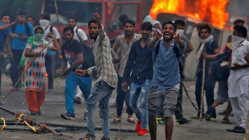 A group of men riot in front of a burning vehicle.