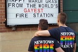 Two firefighters in rainbow T-shirts admire the sign proclaiming Newtown's to be the 'gayest' fire station in the world.