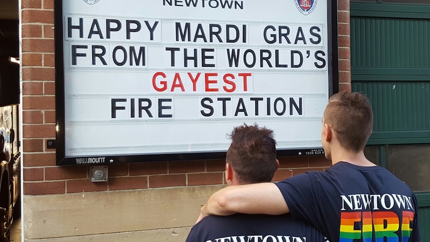 Two firefighters in rainbow T-shirts admire the sign proclaiming Newtown's to be the 'gayest' fire station in the world.