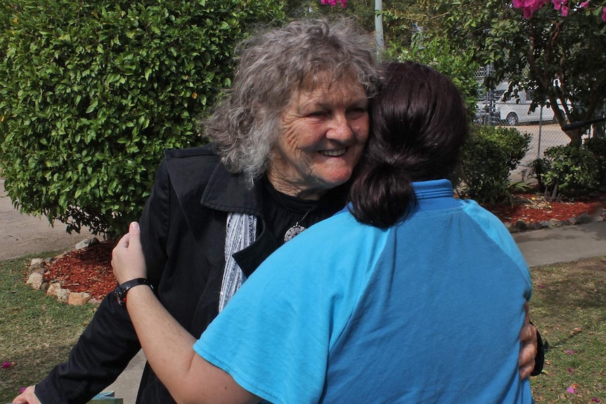 Two women embrace inside a prison, one is wearing prison uniform.