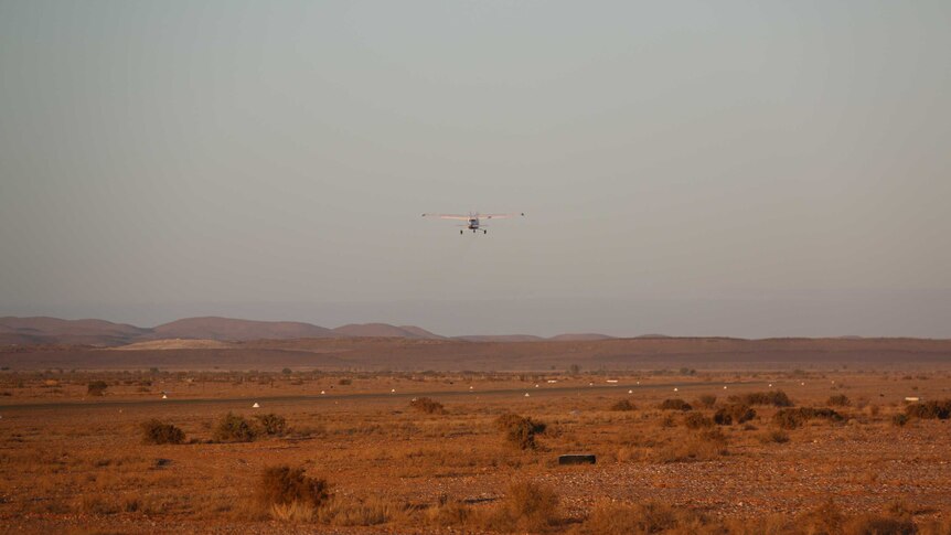 Wide shot of a light plane coming in to land on an airstrip in the Australian outback.