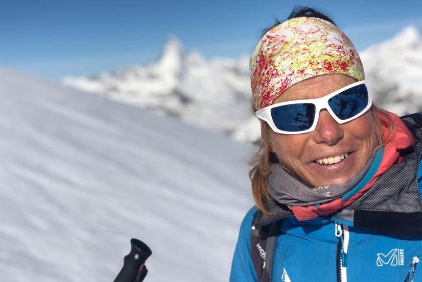 A woman in a bandana stands on asnow-covered mountain.