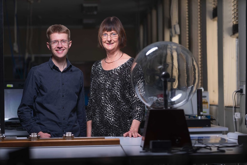 A man and a woman smile, a plasma ball in the foreground.