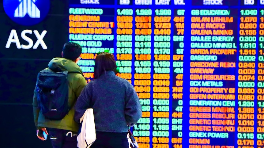 A man and woman, with their baby in a pram, looking at the ASX stock market boards in Sydney.