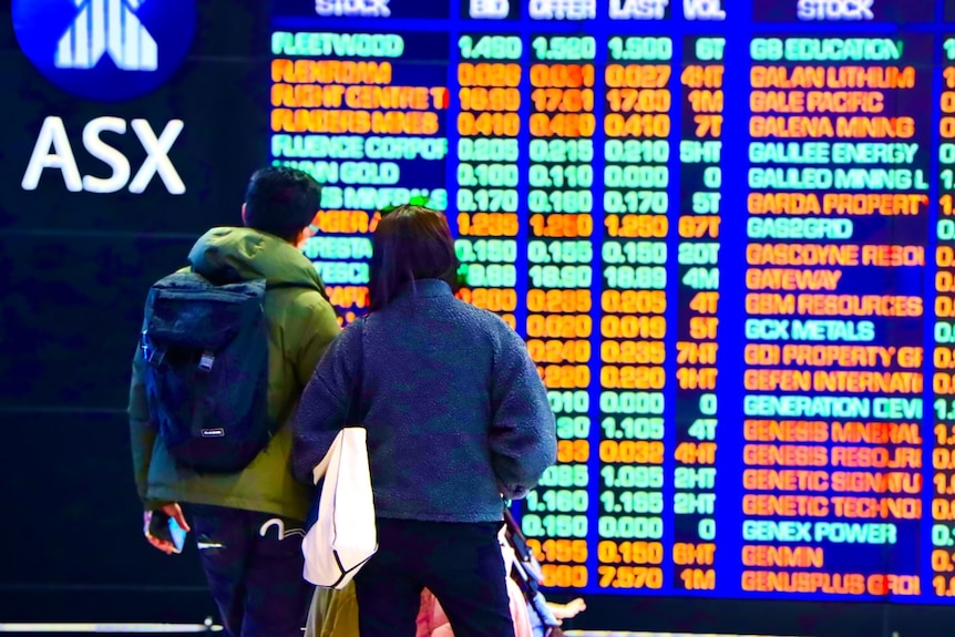 A man and woman, with their baby in a pram, looking at the ASX stock market boards in Sydney.