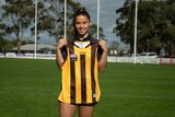 Dominque Carbone hold up a Hawthorn jersey on a football oval.