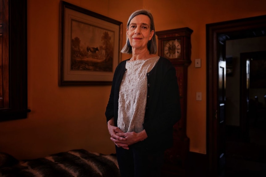 A woman stands in a darkened interior with a grandfather clock in the background.