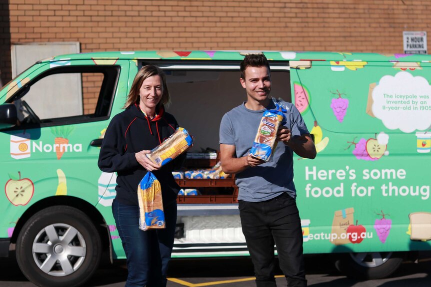 A woman and man hold bread loaves in front of the Eat Up van