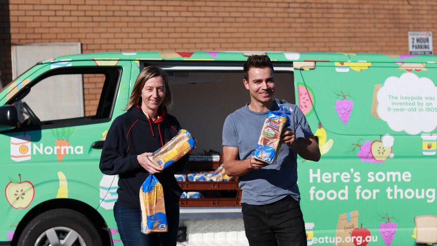 A woman and man hold bread loaves in front of the Eat Up van