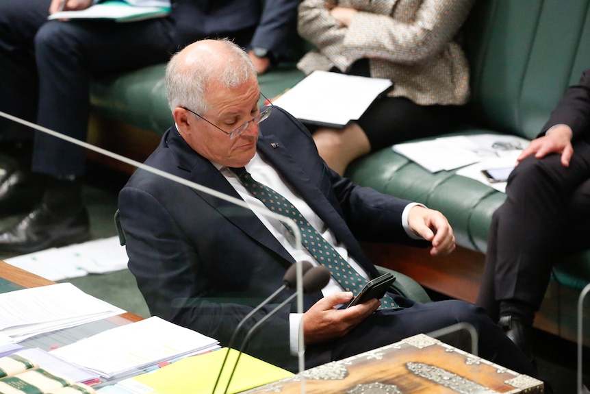 Scott Morrison looks at his phone in question time