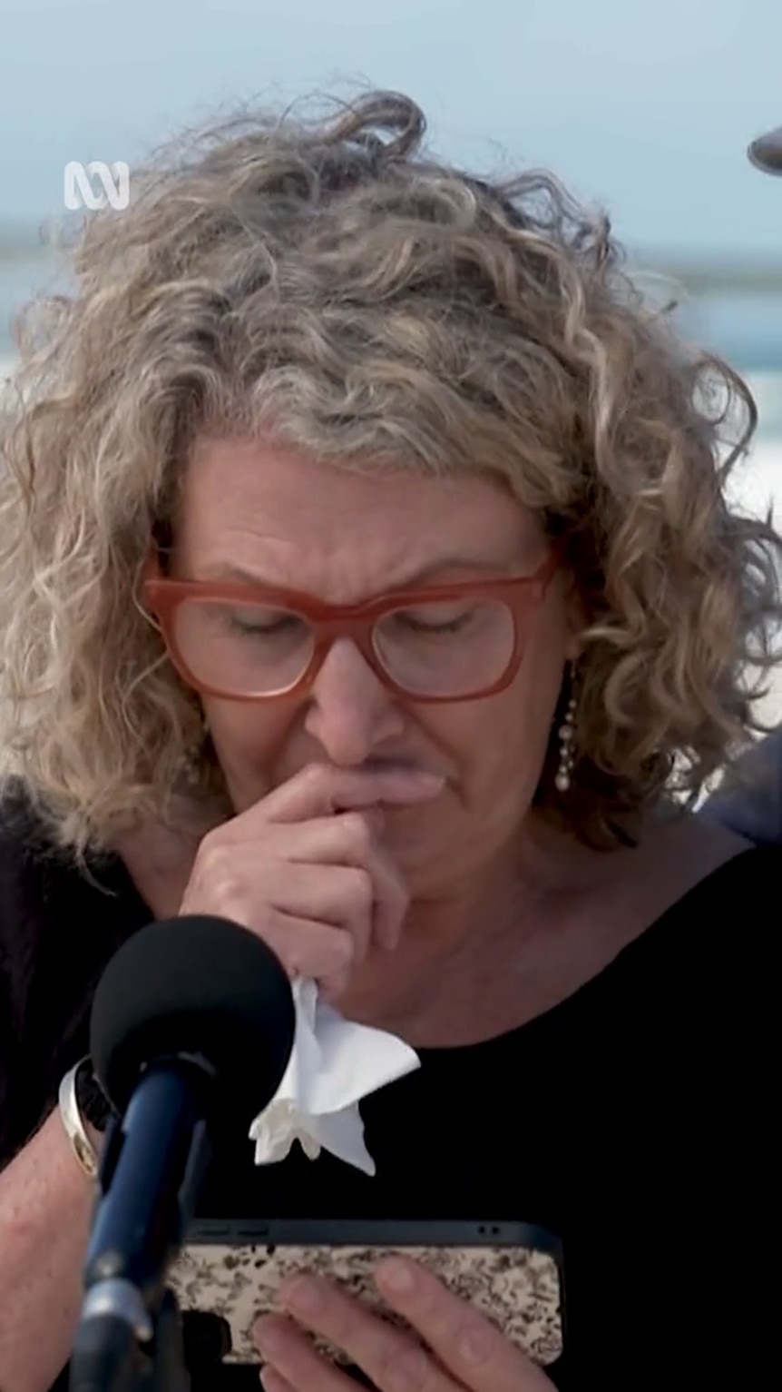 A middle-aged white woman with curly hair holds a tissue to her face as she looks down
