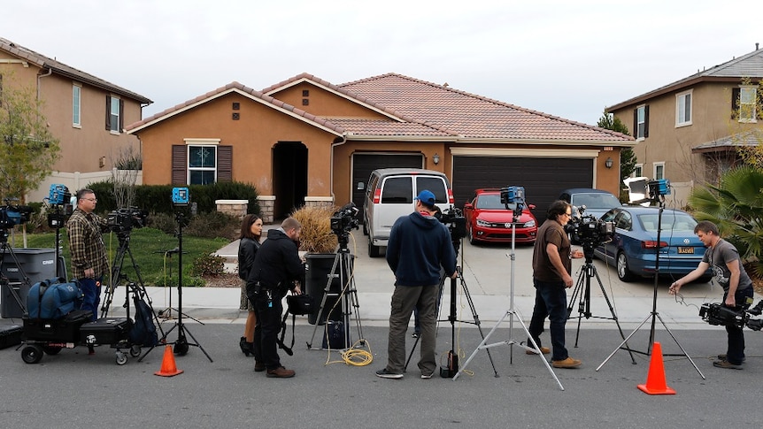 Reporters stand outside a single-story brick house.
