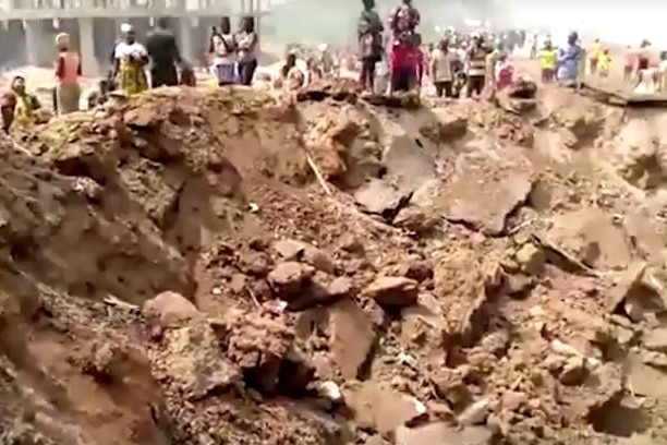 People standing around a massive crater after an explosion in the street.