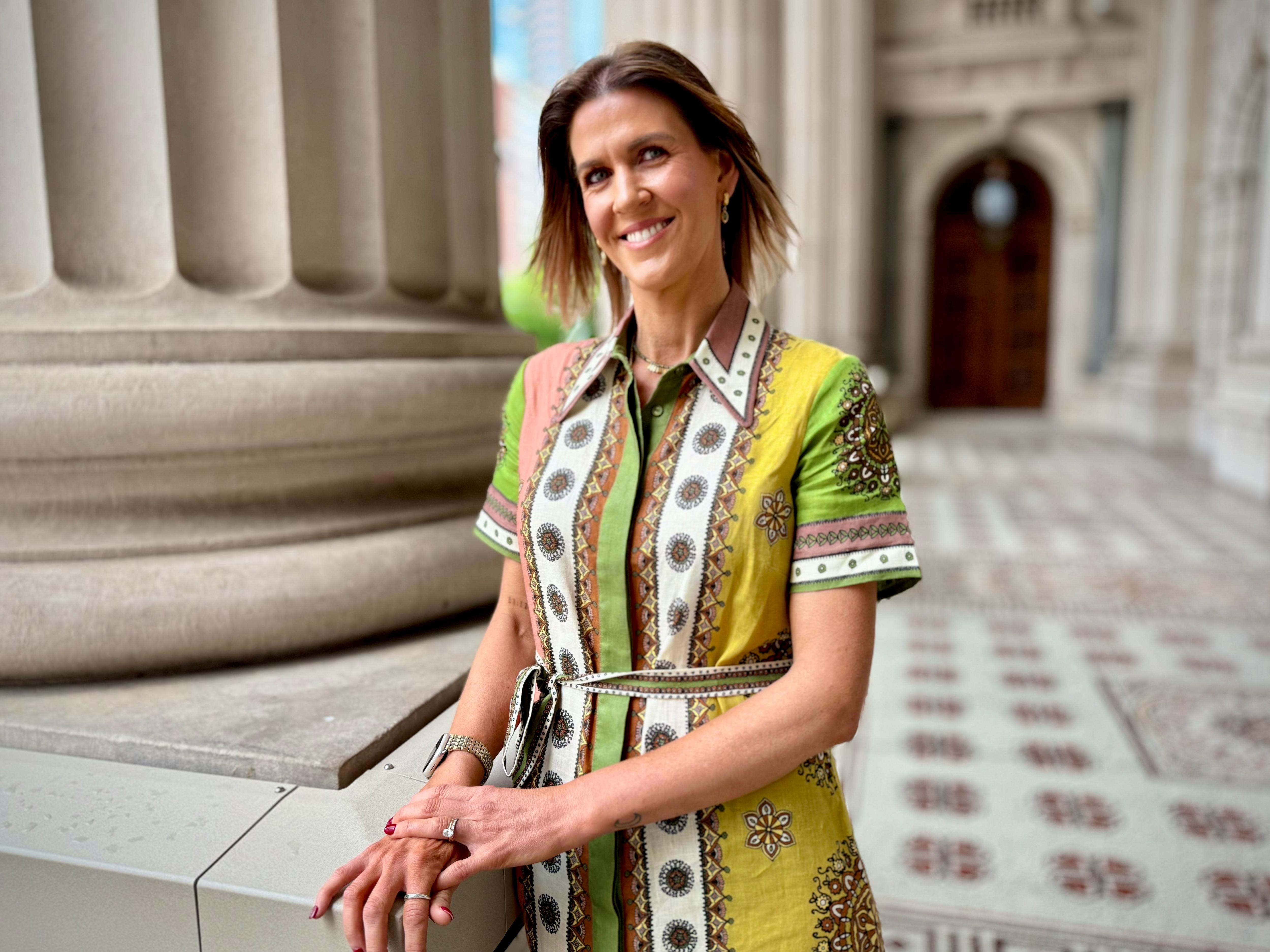 Woman in colourful dress smiles at the camera outside parliament.
