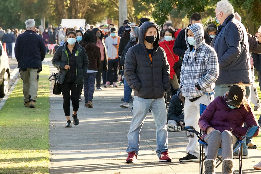 People wearing masks wait in line on a sunny day.