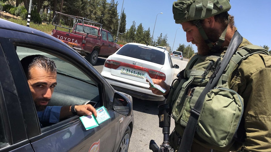 A soldier checks a Palestinian man's ID at a checkpoint near Gush Etzion