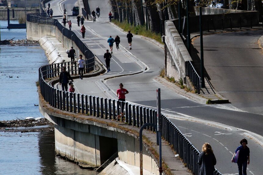 People jog and walk on a Paris street along the Seine river.