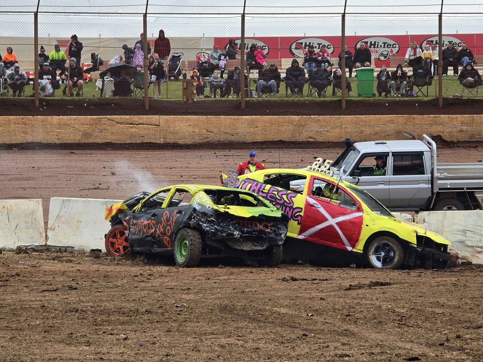 Two demolition derby cars crash near a concrete barrier. 
