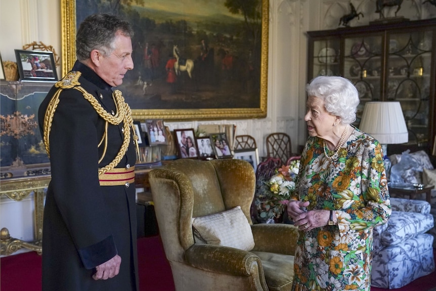 Королева в цветочном платье разговаривает с мужчиной в форме в Виндзорском замке.