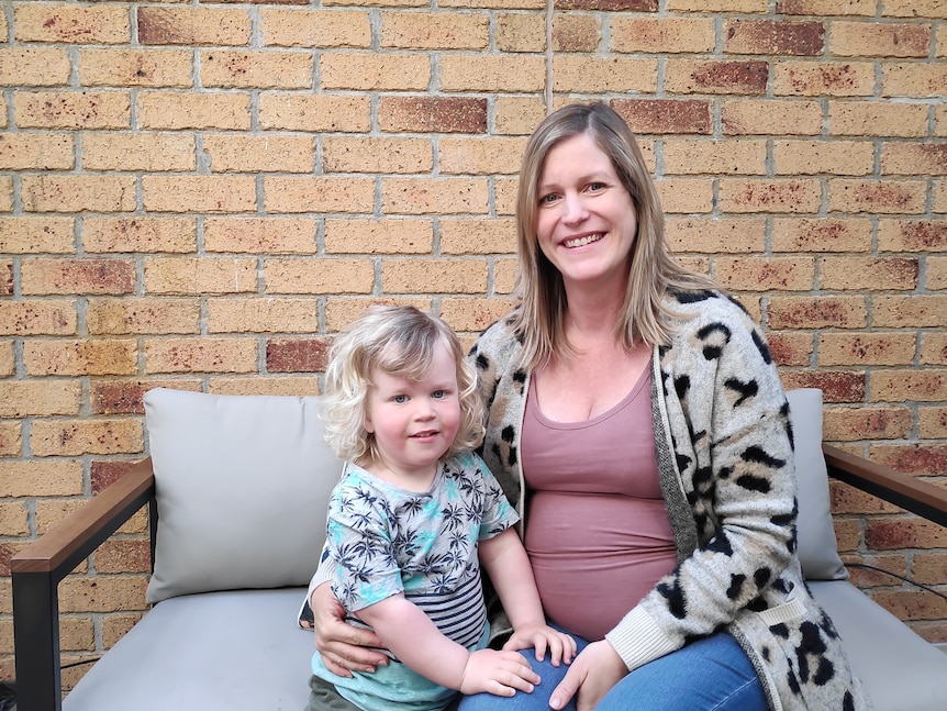 A woman sitting on a bench with her young son, both are smiling