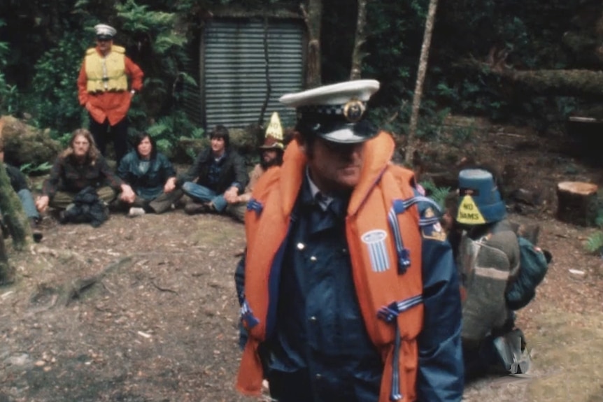 A police officer watches over a group of protesters sitting on the ground.