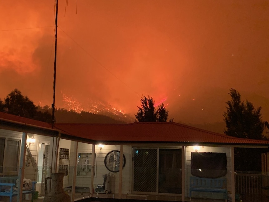 A home with flames and orange smoke behind it.