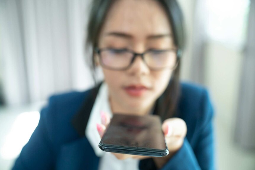 Photo of an out of focus woman holding a phone in front of her and speaking into it.