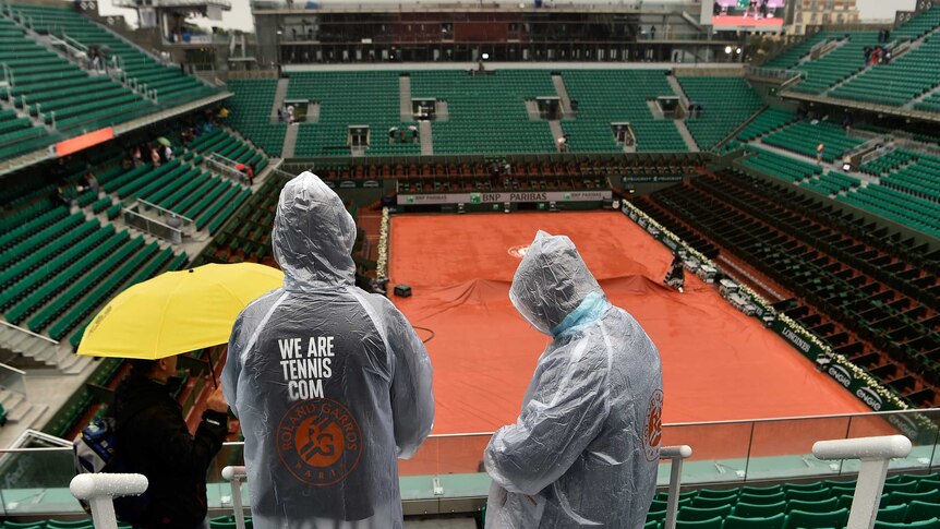 Spectators in ponchos look on as rain interrupts French Open