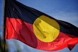 An Indigenous flag flaps in the wind against a blue sky background