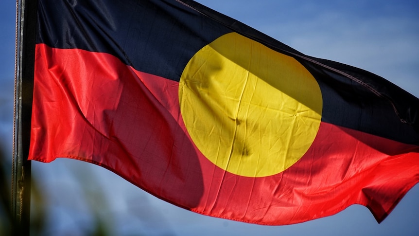 An Indigenous flag flaps in the wind against a blue sky background