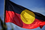 A close up shot of the Aboriginal flag flying with blue sky in the background.