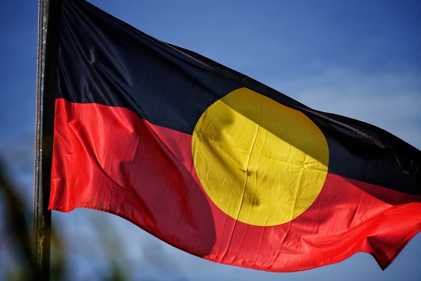 The Aboriginal flag flies against a blue sky.