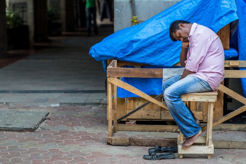 An Indian man sitting and sleeping outside his sales booth early in the morning in south Mumbai, India