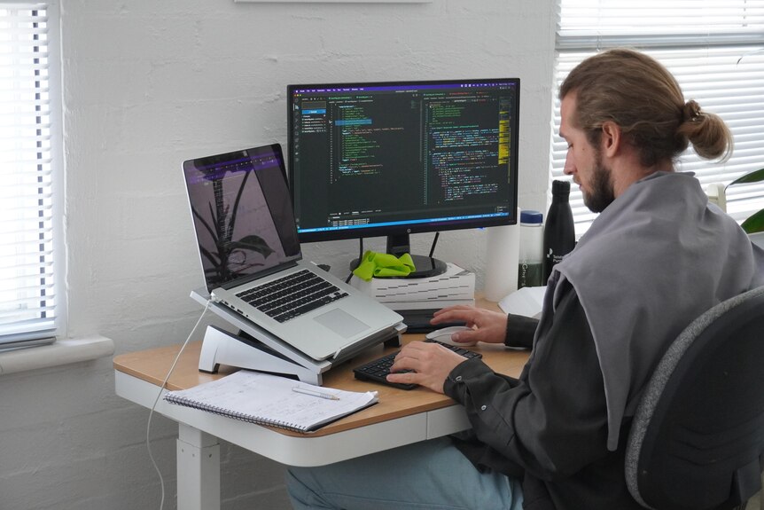 A man sits in front of multiple computer screens programming. 