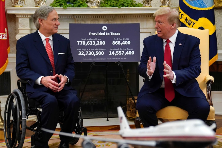 Donald Trump sits in a yellow chair in the Oval Office next to Greg Abbott, who uses a wheelchair. There is a poster behind them