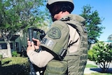 A police officer carries an automatic weapon while wearing body armour and a helmet.