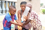 An African woman helps her children wash their hands with a bottle of water.