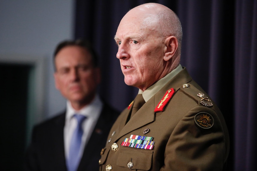 Frewen, a bald man, is mid-speech, wearing an army military uniform.