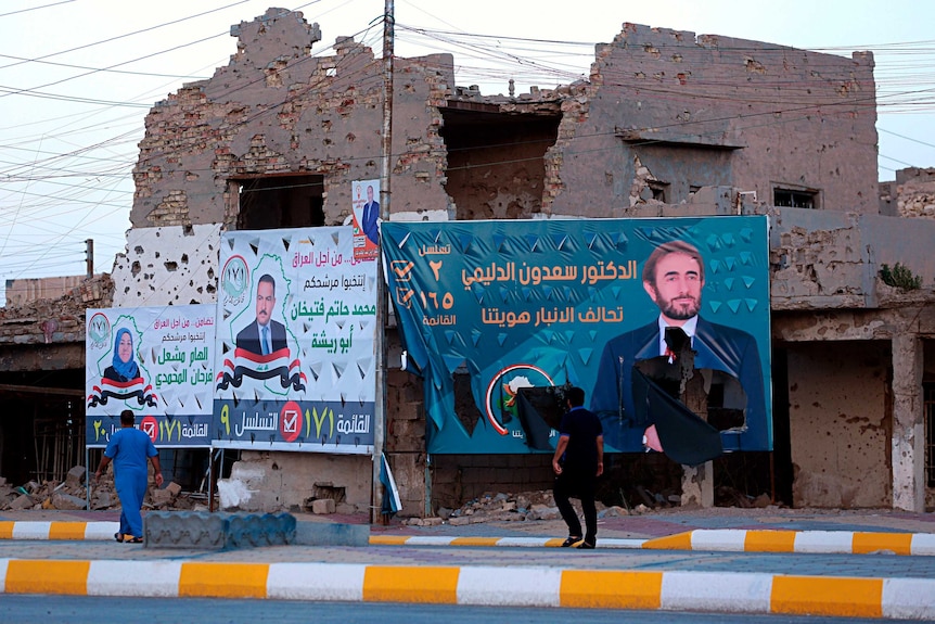 Campaign posters for parliamentary elections are displayed near destroyed buildings