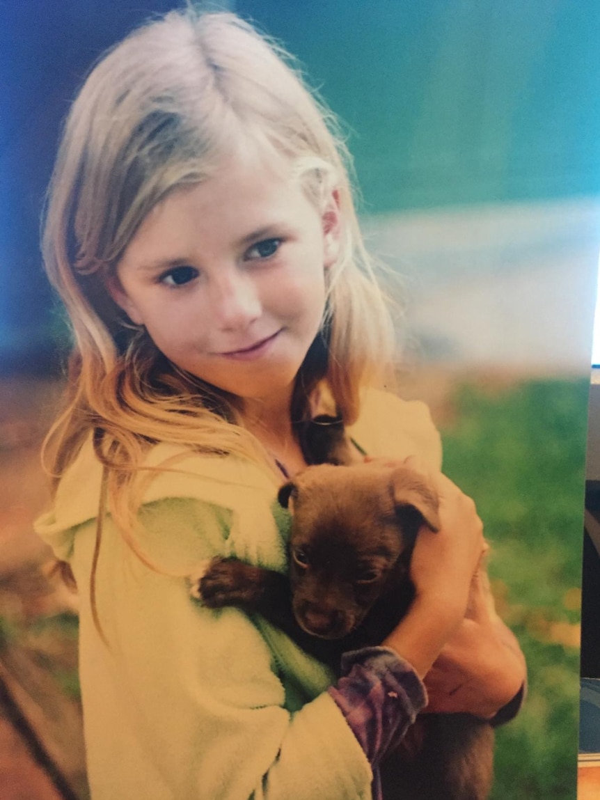 A childhood picture of Alexandra Henderson as a young girl, wearing a green bathrobe and holding a puppy.