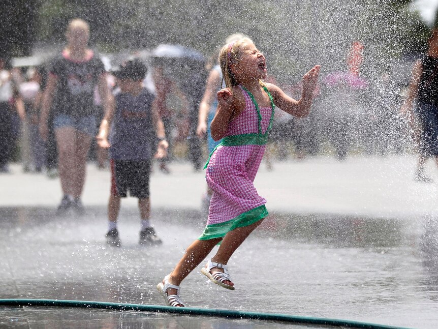 Children cool themselves with a spray of water leaking from a hose during a heatwave in the US.