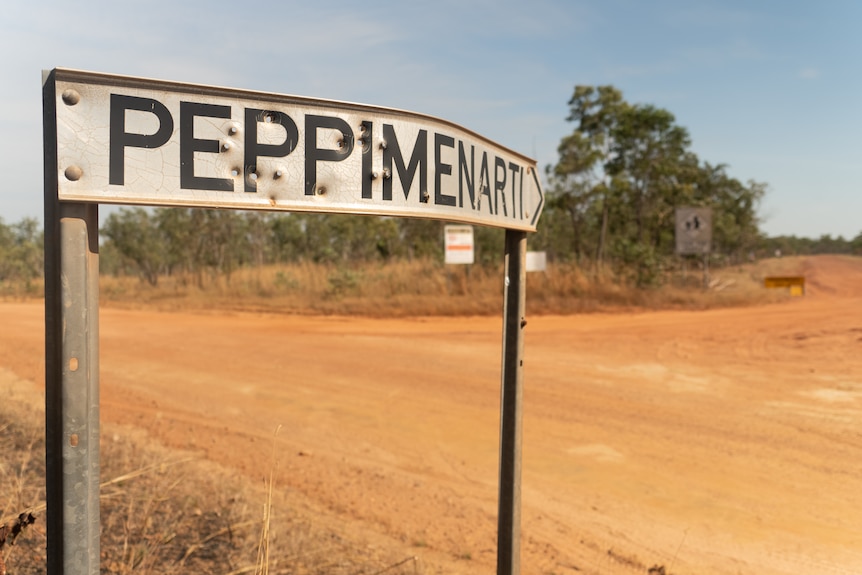 A roadside sign reading "Peppimenarti" riddled with holes, on the side of a red dirt road.