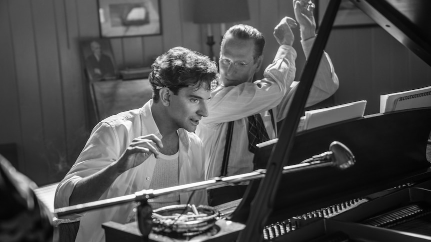 Black and white image of Bradley Cooper sitting at a piano. 