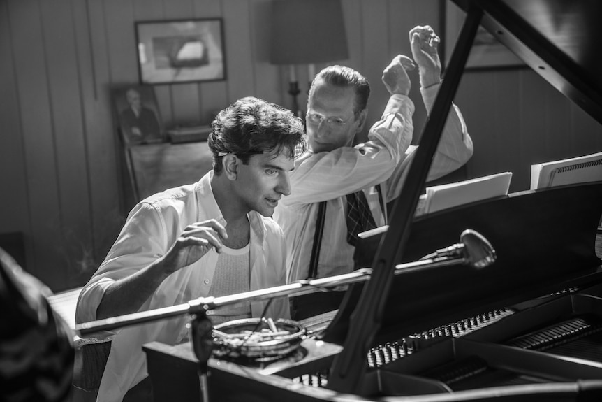 Black and white image of Bradley Cooper sitting at a piano. 